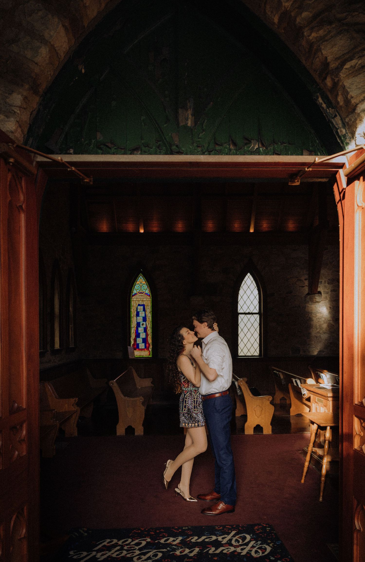 A couple dancing in a dimly lit stone church interior with arched windows.