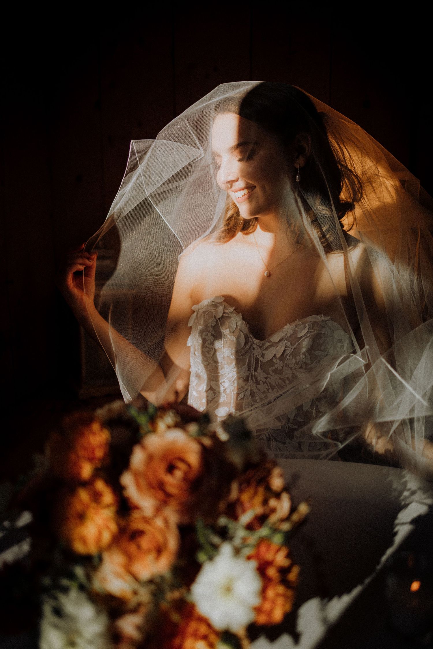 Ethereal bridal portrait with flowing veil and autumn-colored flowers in moody lighting.
