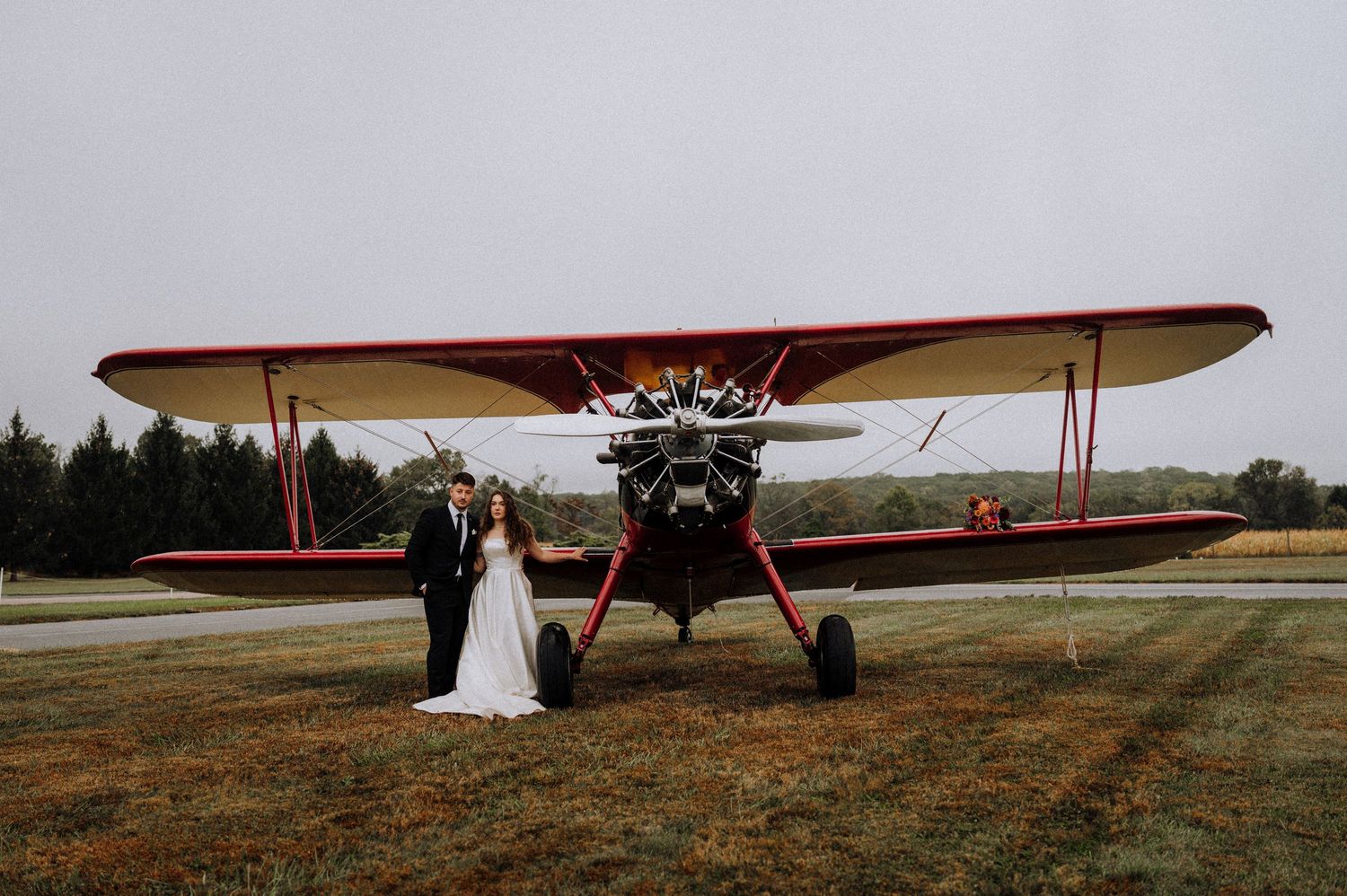 A classic wedding portrait featuring a vintage red biplane as a stunning backdrop.