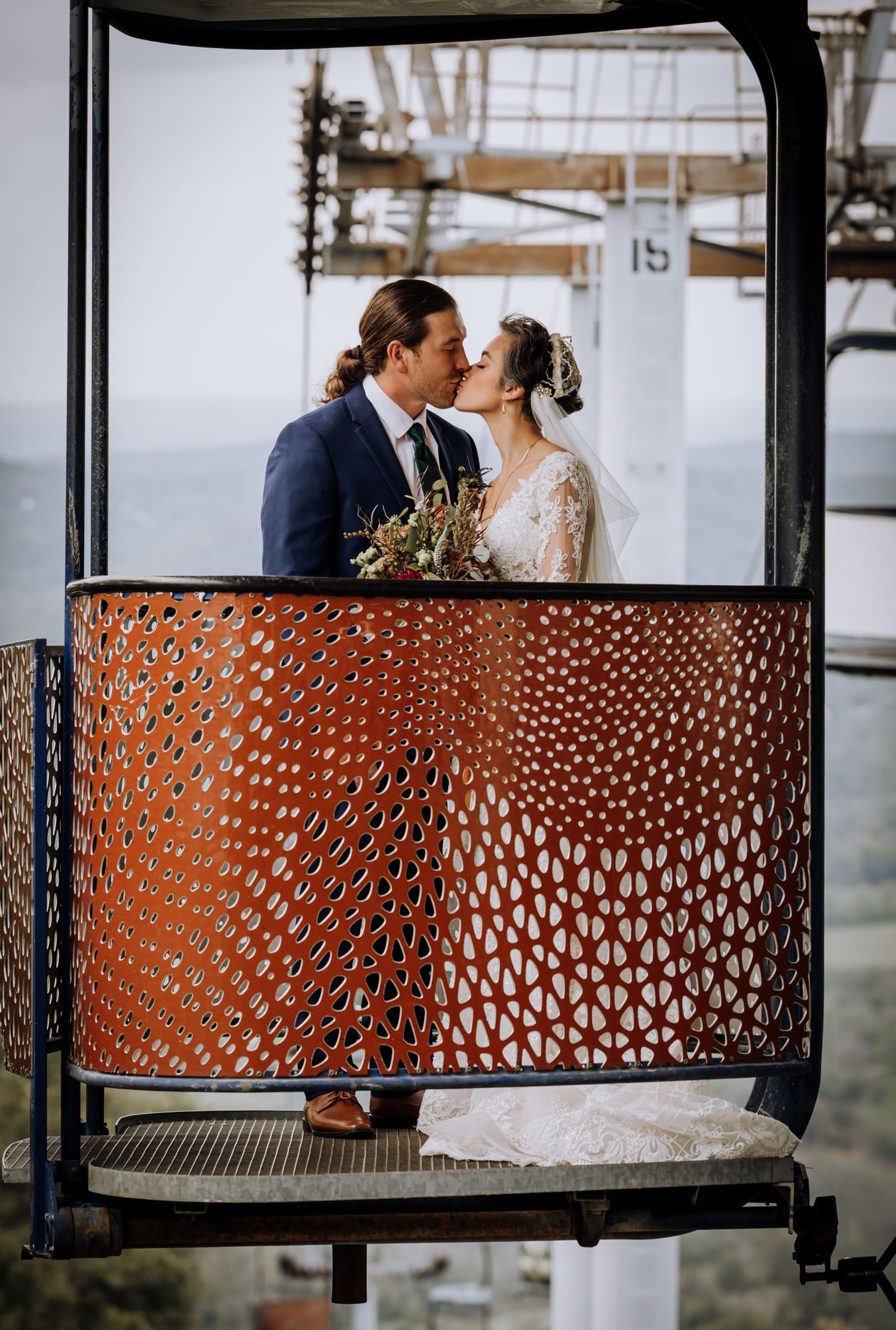 Couple shares romantic moments behind decorative metal railing with mountain views.