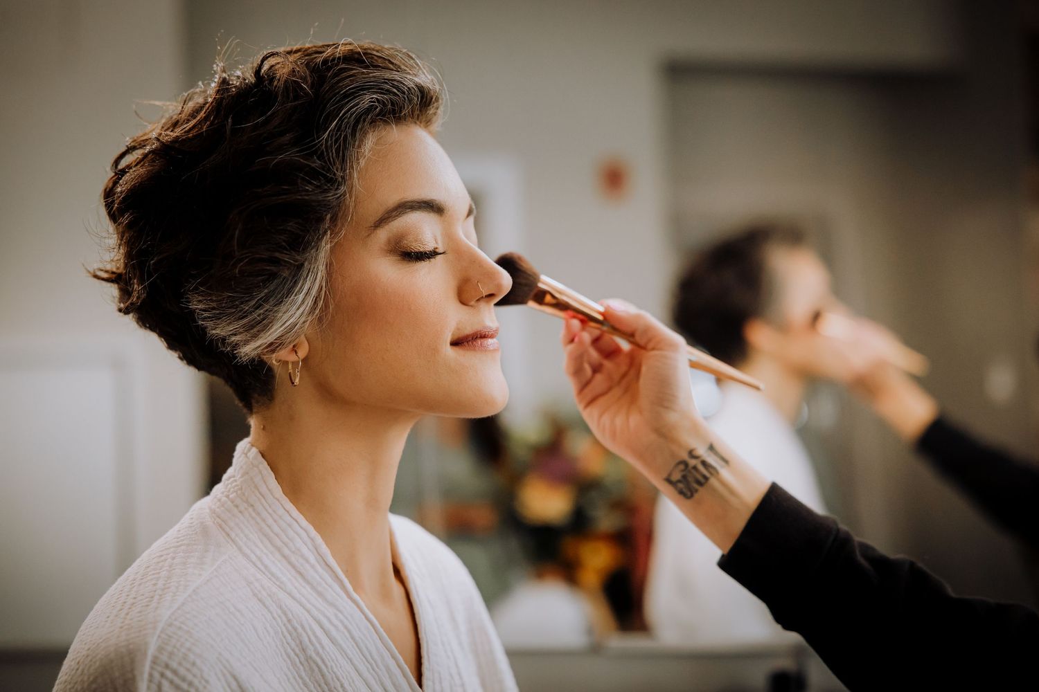 Professional makeup artist applies cosmetics to a person wearing a white robe during wedding preparations.