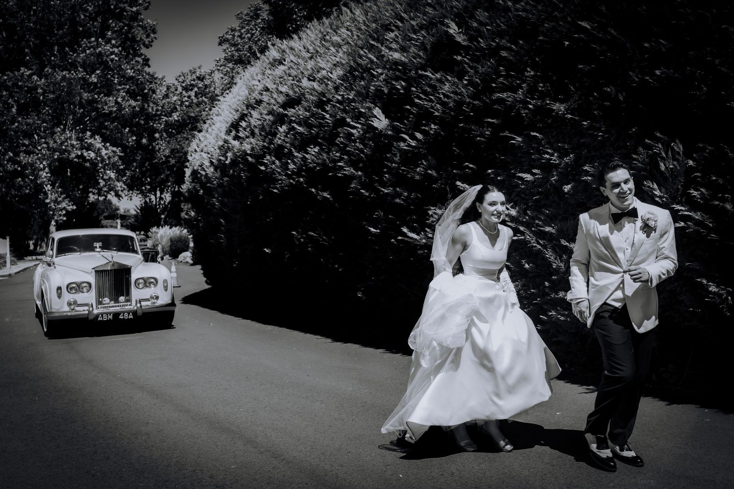 Black and white wedding photography captures elegant moments with vintage car and formal attire.