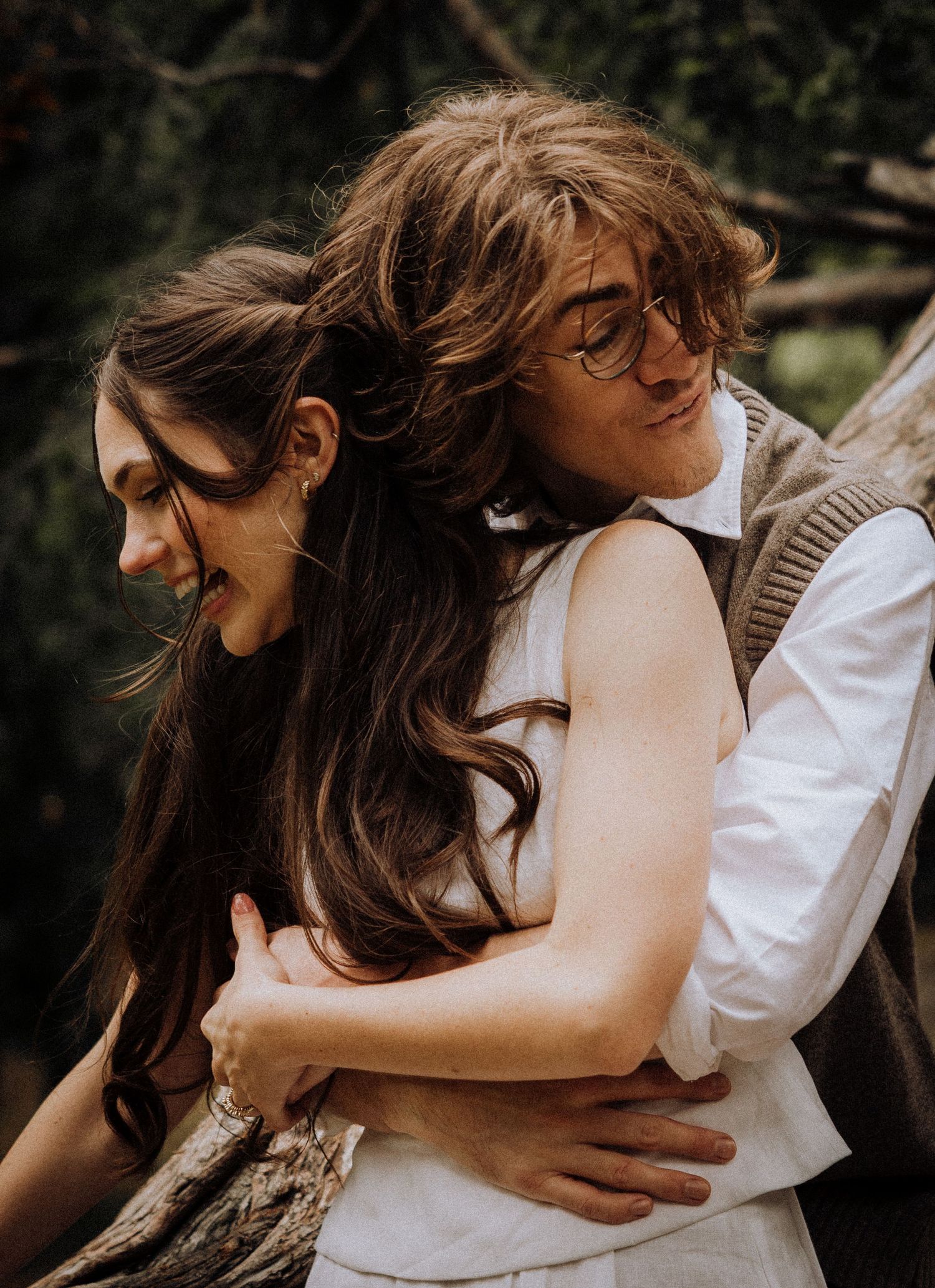 Intimate embrace captured in soft lighting among trees.