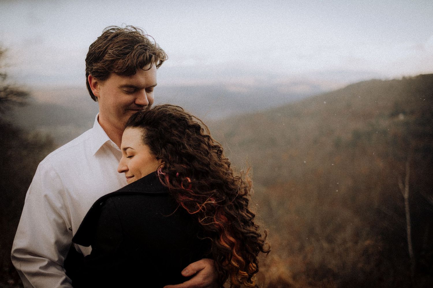 Couple sharing intimate moment against scenic mountain vista backdrop.