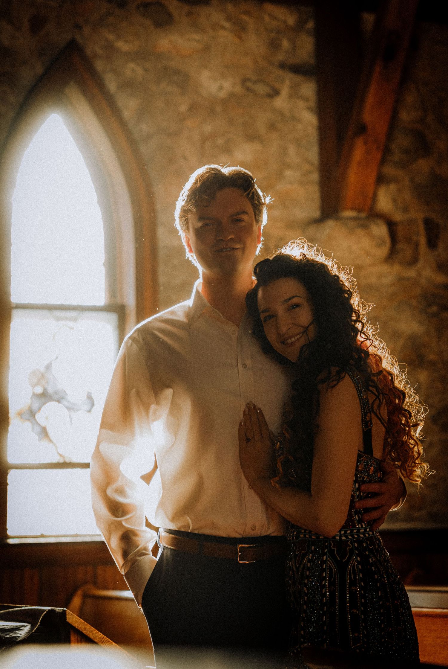 A romantic portrait in front of an arched church window with sunlight streaming in.