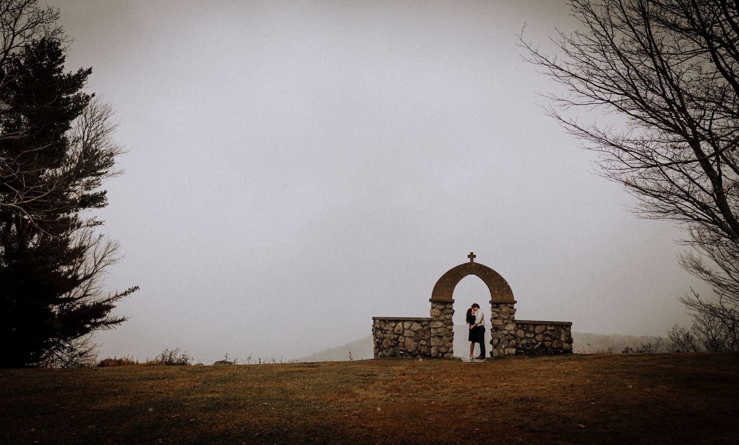 A foggy landscape view featuring a small chapel with stone archways on a hilltop.