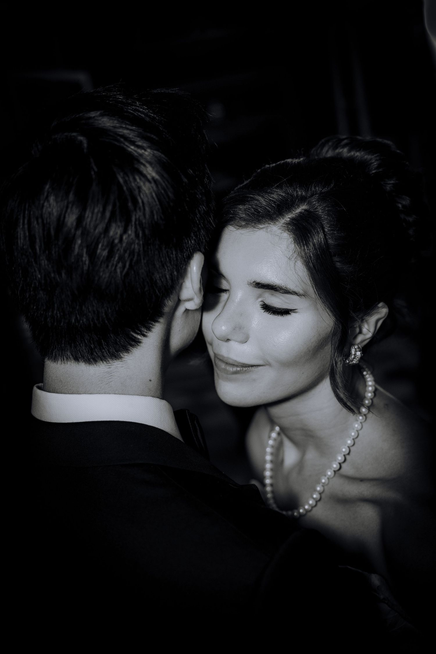 Black and white photo of a couple dancing closely, woman wearing pearl necklace and earrings smiling softly.