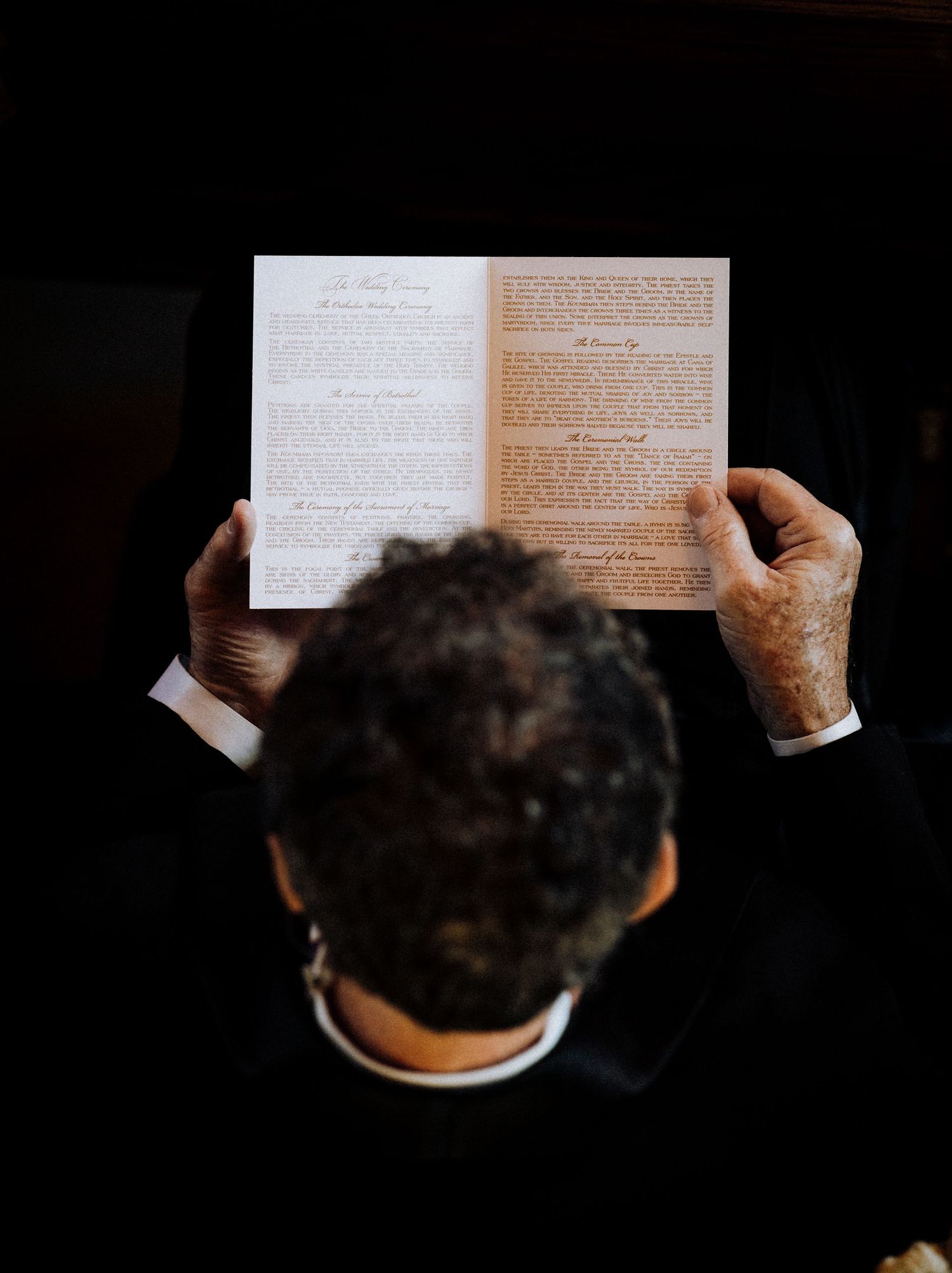 Overhead view of a man in a suit reading a wedding ceremony program with elegant script text.