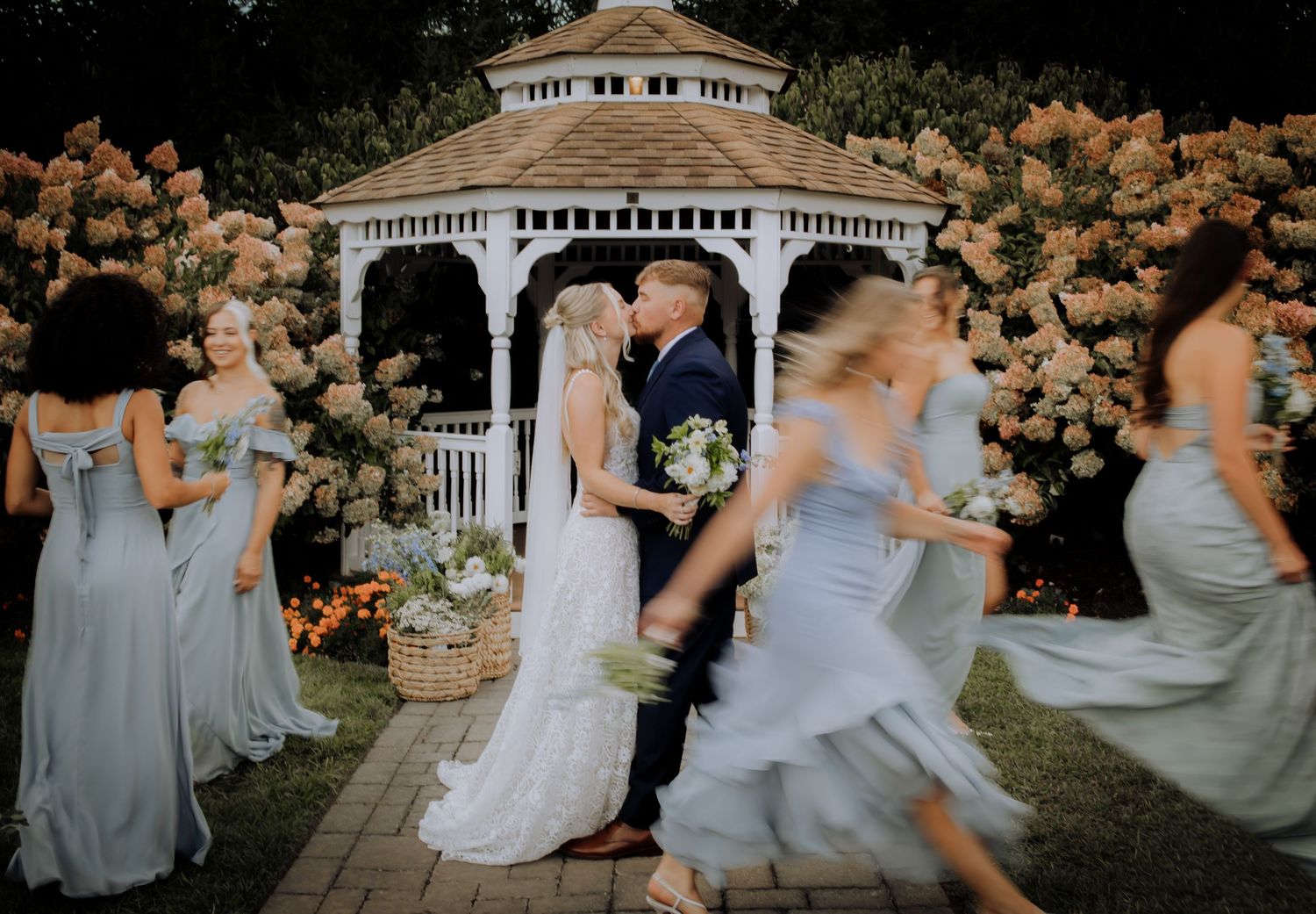 Wedding party poses together in front of a white gazebo with light blue bridesmaid dresses.