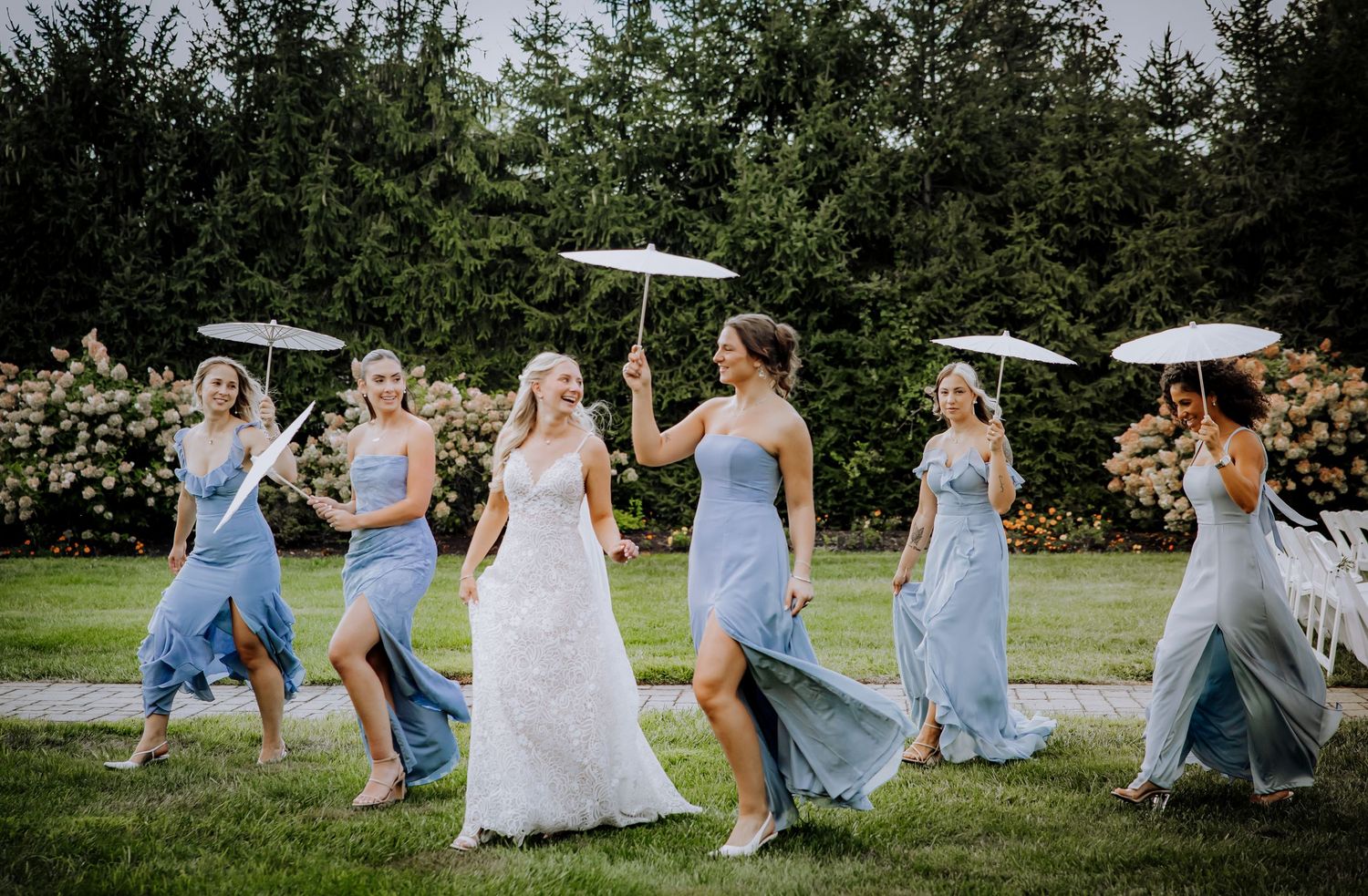 Wedding party members in light blue dresses dance and celebrate on a grassy lawn.Editorial and Cinematic Wedding photos