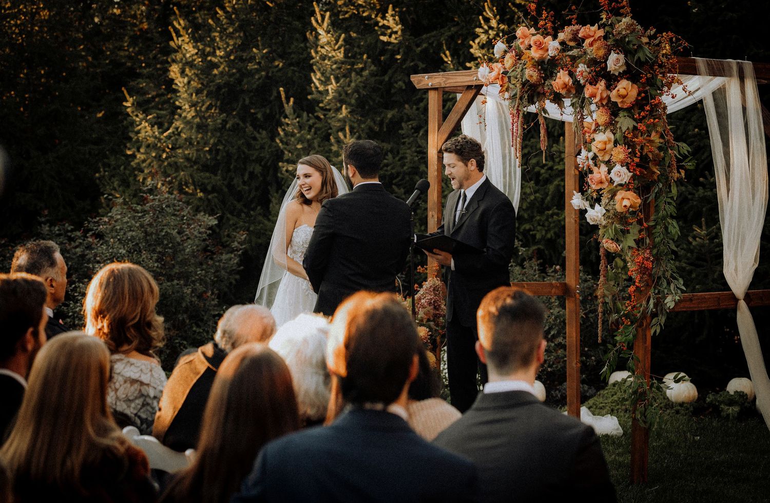 Romantic outdoor wedding ceremony setup with rustic wooden arch decorated in autumn florals at sunset.