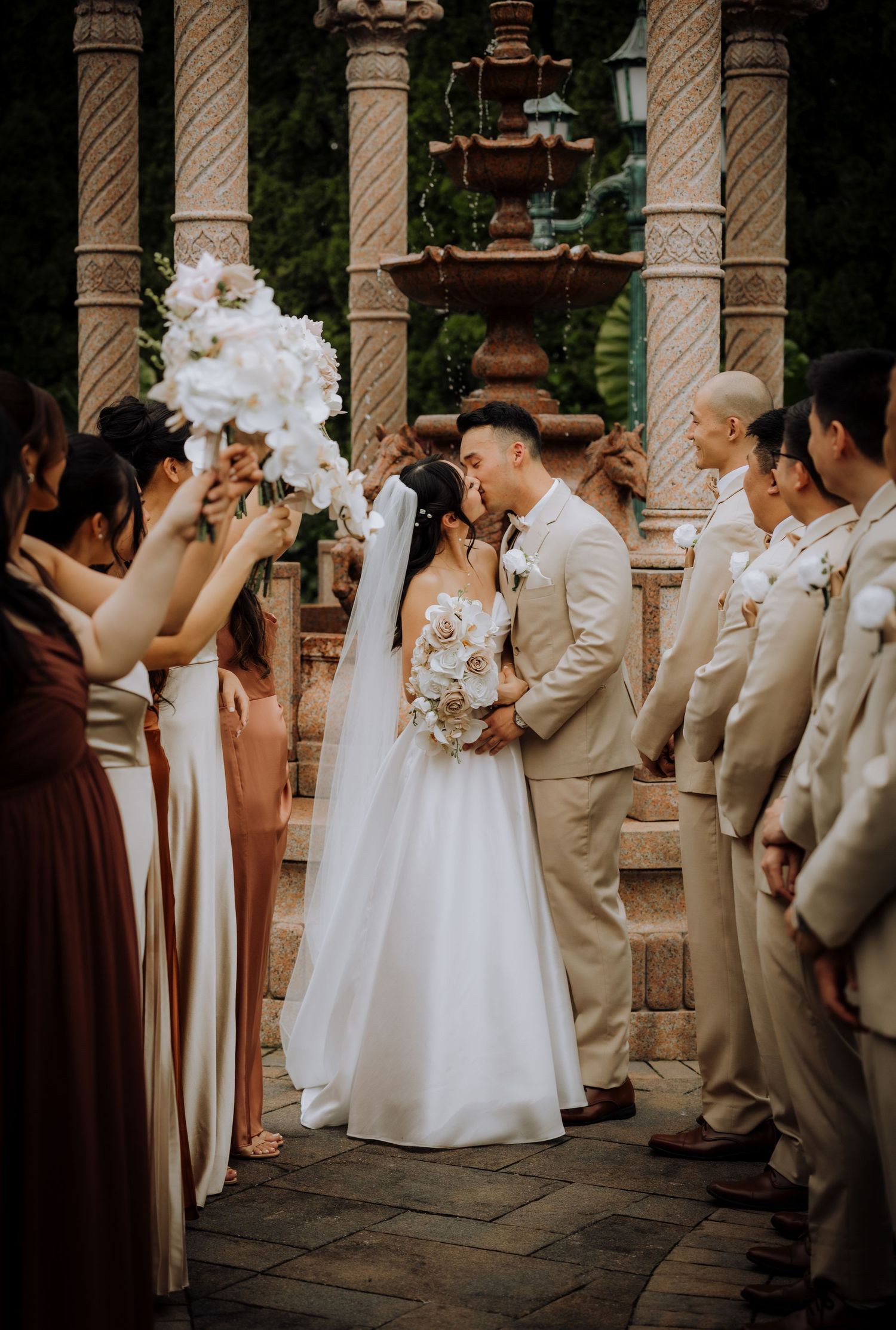 Wedding party gathers under stone columns during outdoor ceremony.