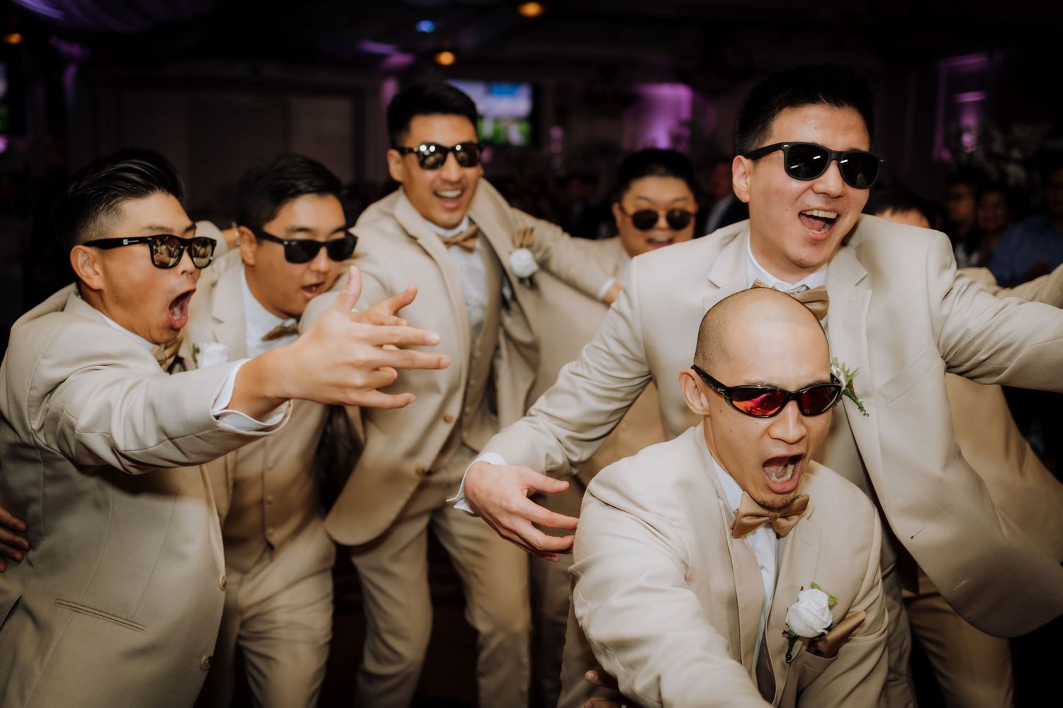 Wedding party wearing sunglasses and light-colored suits dancing at reception.