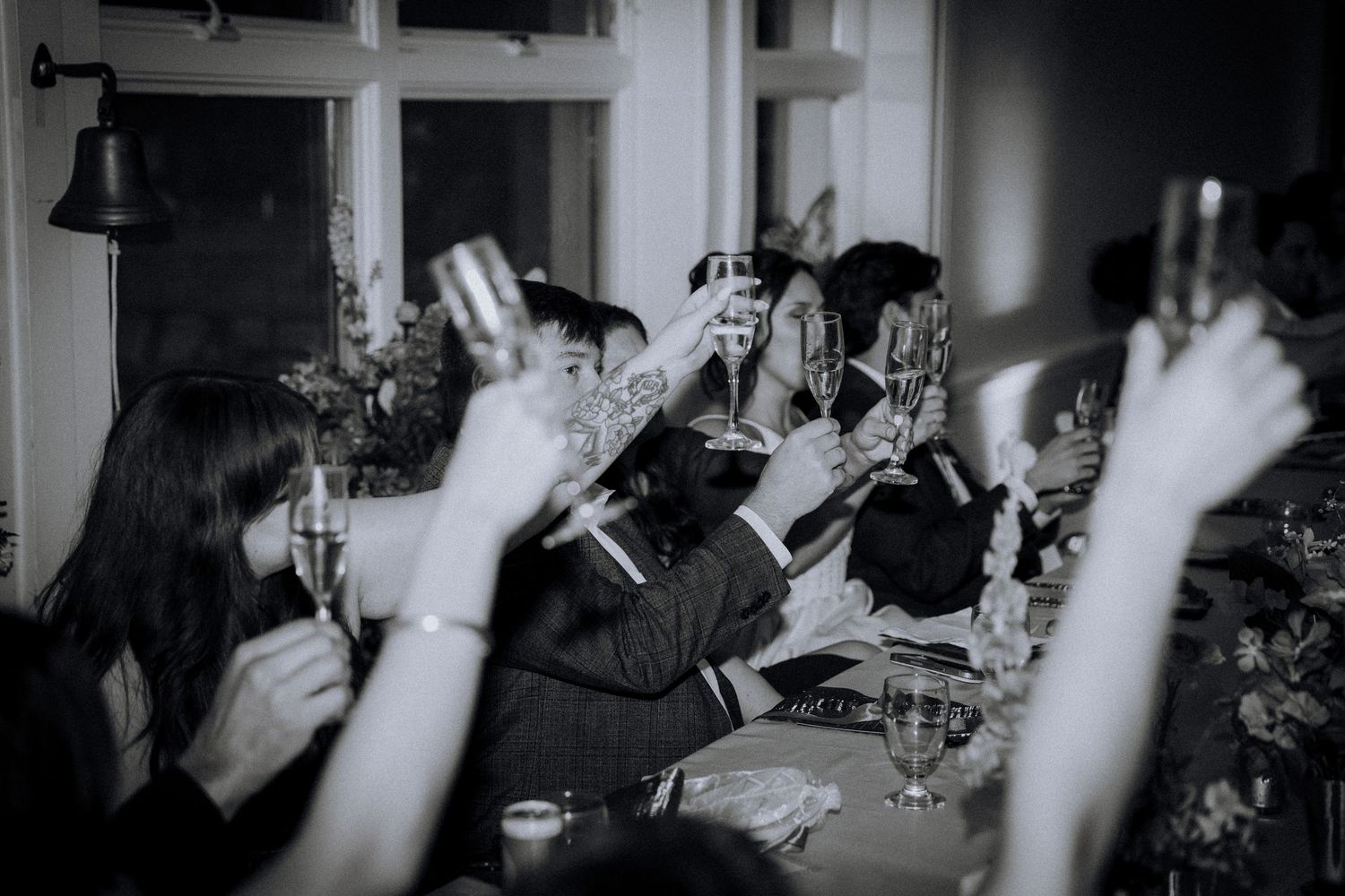 Black and white photo of guests raising champagne glasses in a toast at an elegant dinner party celebration.