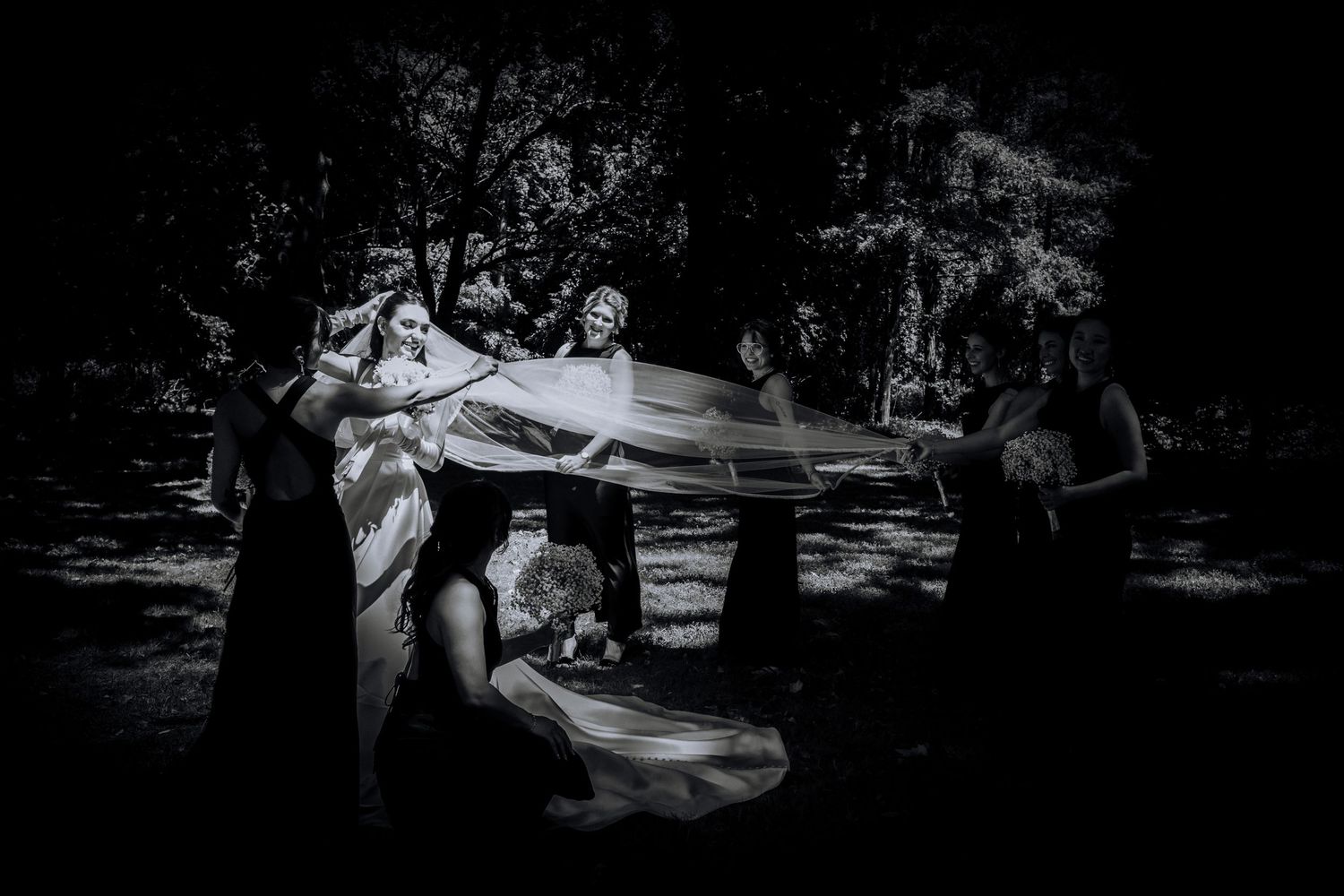 Black and white wedding photo showing playful moment with bride's dress in outdoor setting.