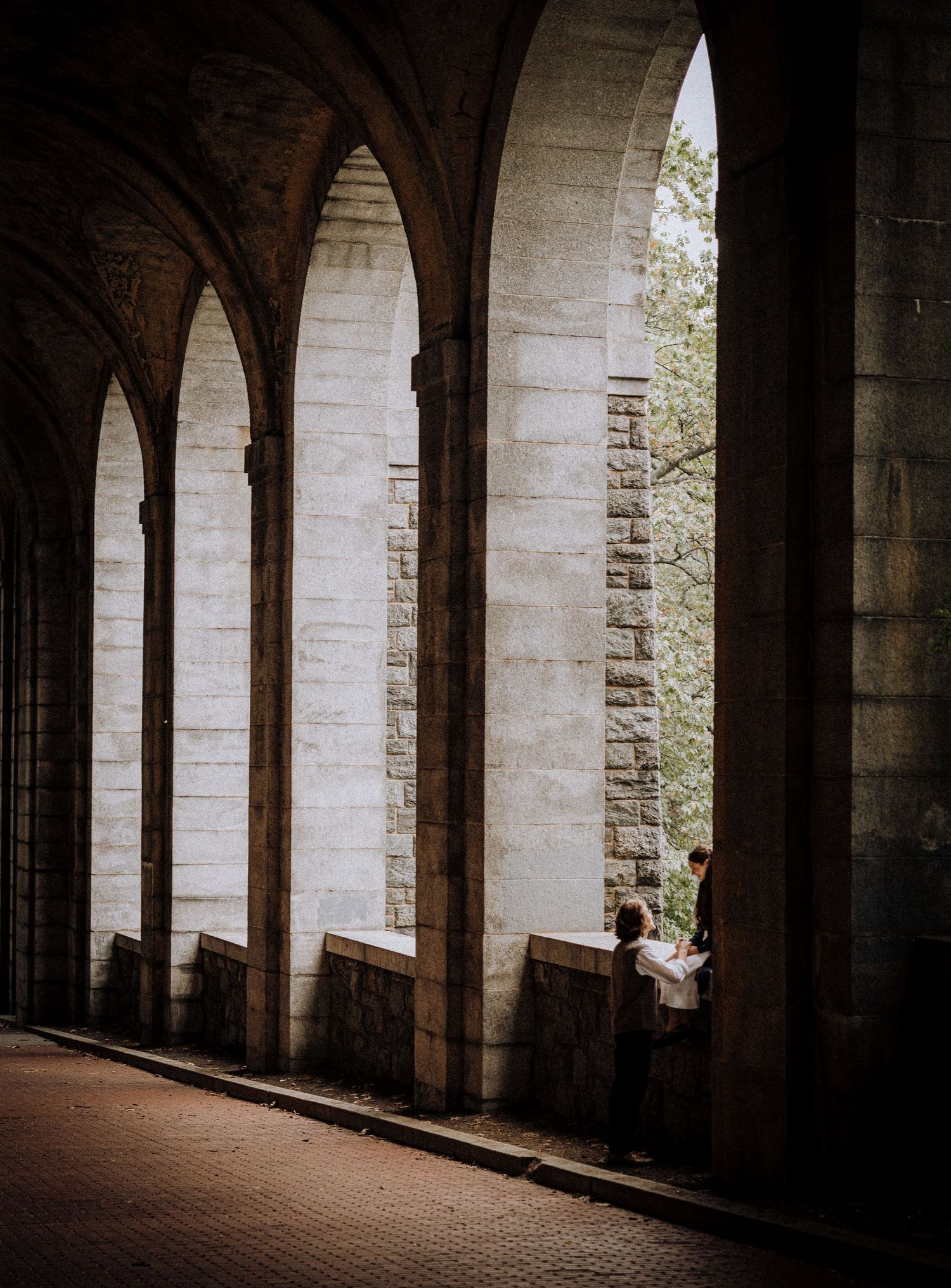 A dark stone archway corridor with natural light streaming through windows.