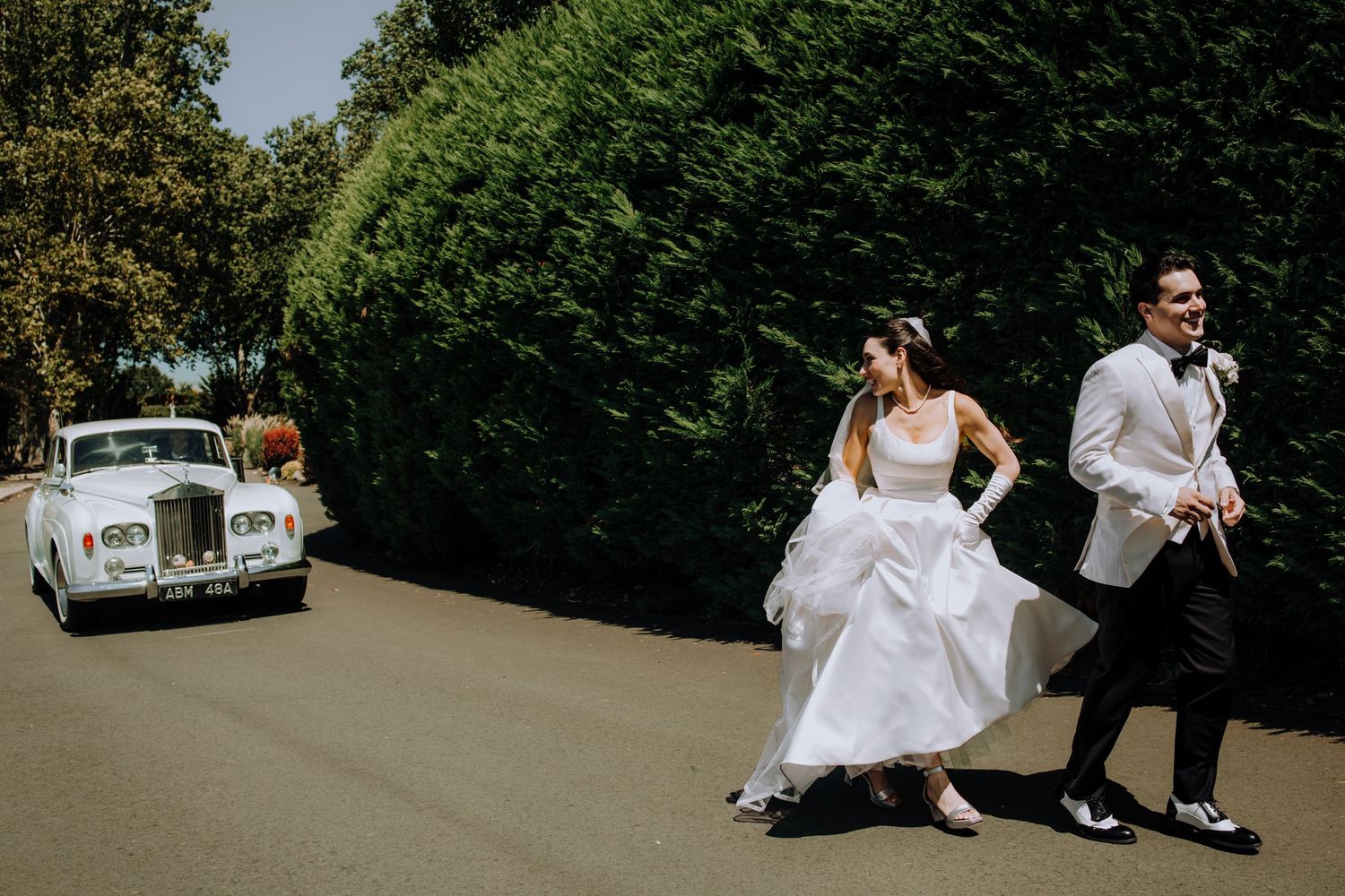 Wedding party relaxes outdoors in formal attire with vintage car visible in background.Editorial and Cinematic Wedding photos