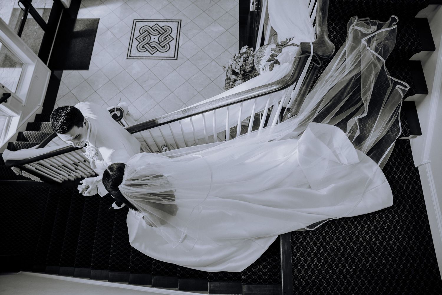 Black and white aerial view of a bride in a flowing white gown and veil descending an elegant staircase.Editorial and Cinematic Wedding phot