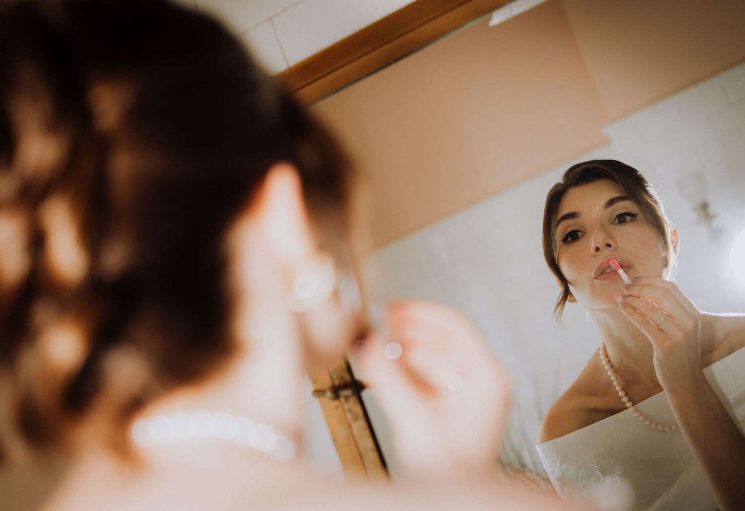 Woman applying lipstick while looking in bathroom mirror, beauty makeup routine preparation.
