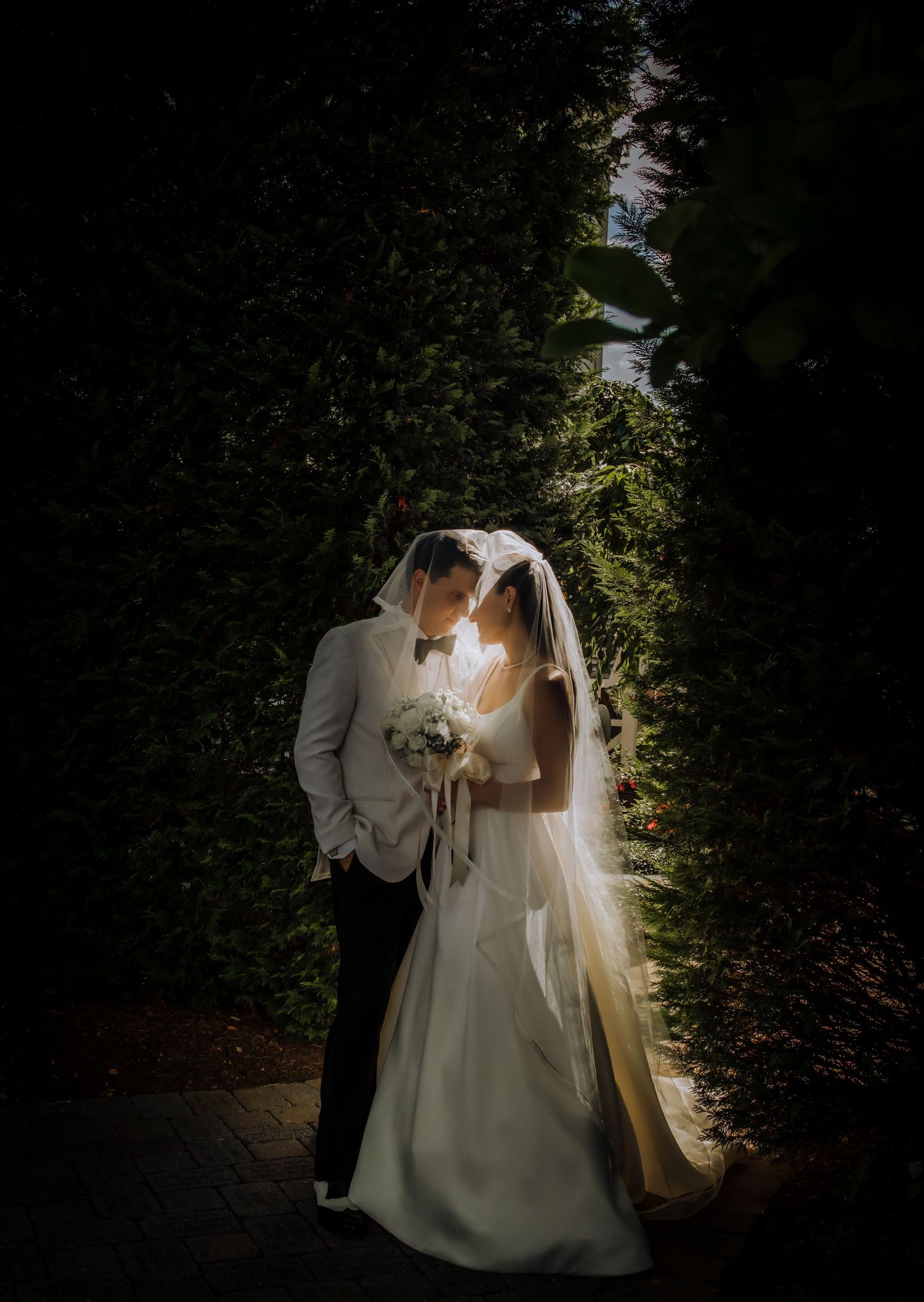 Newlyweds in white attire pose together in a garden setting.