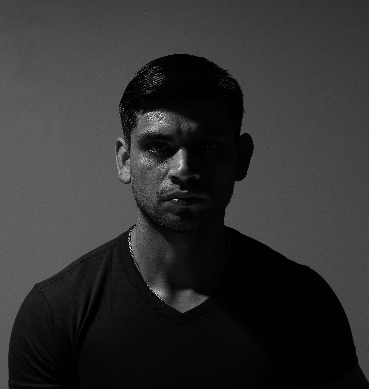 Black and white portrait of a muscular young man in a dark t-shirt against a neutral background.
