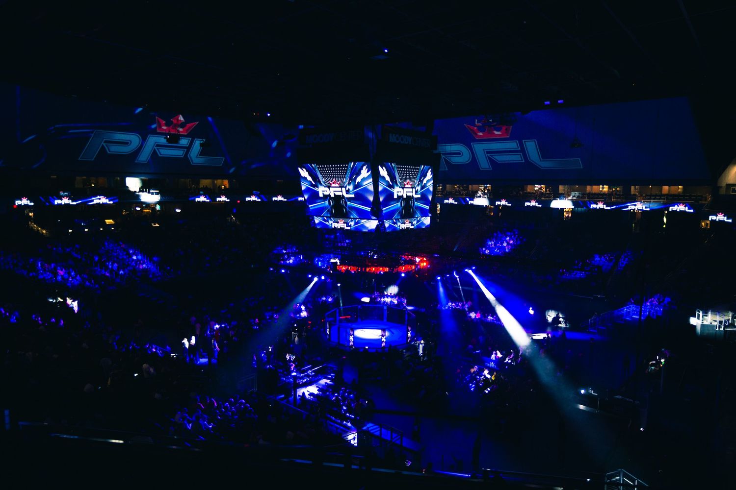 Aerial view of a PFL MMA arena lit with blue lights, showcasing the octagon and packed crowd at a live event.