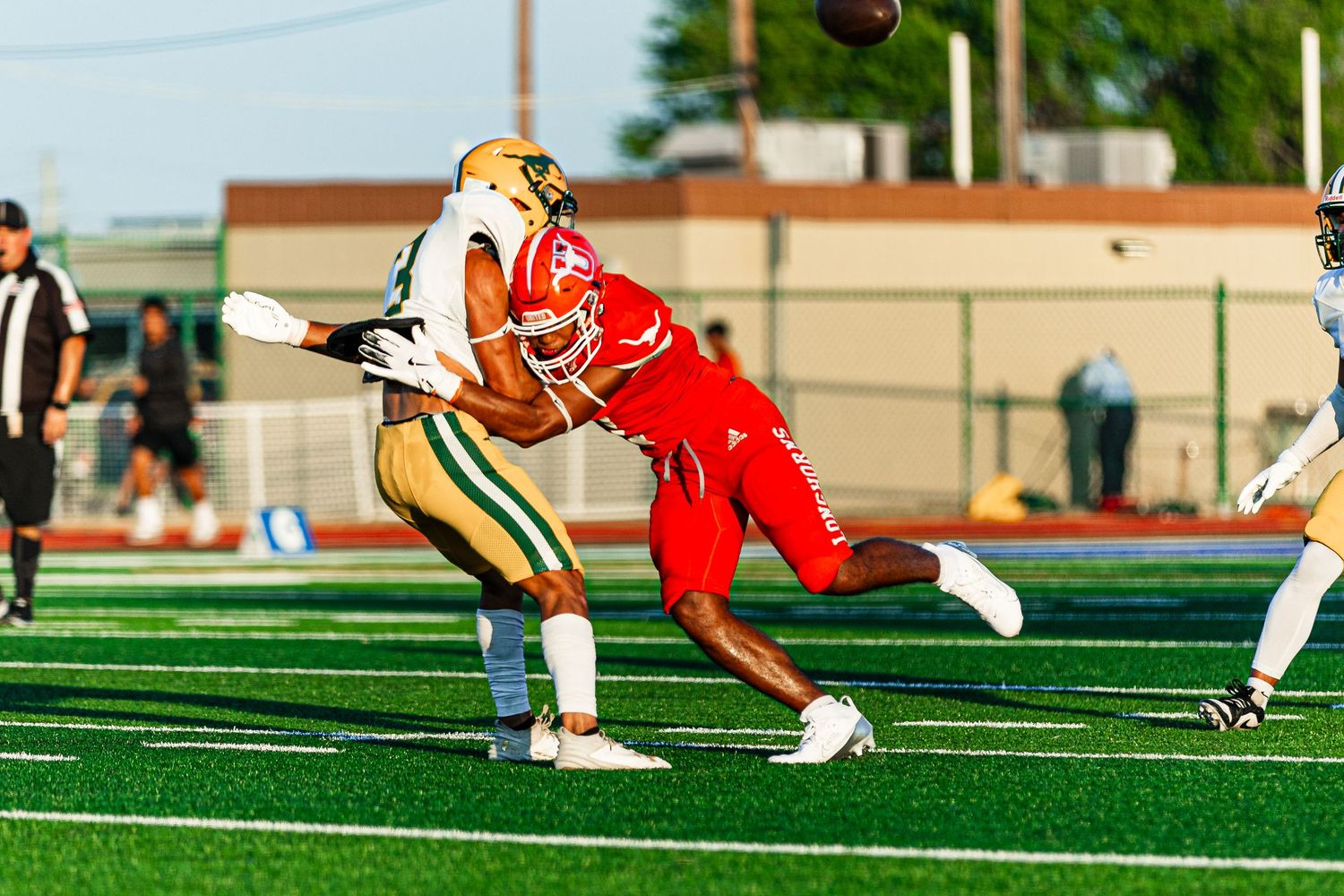 Two football players compete for a pass during a high school game on a green turf field under stadium lights.