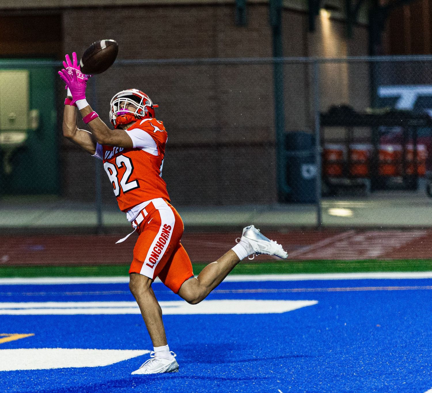 Football player #82 in orange uniform leaps to catch a pass during a night game under stadium lights.