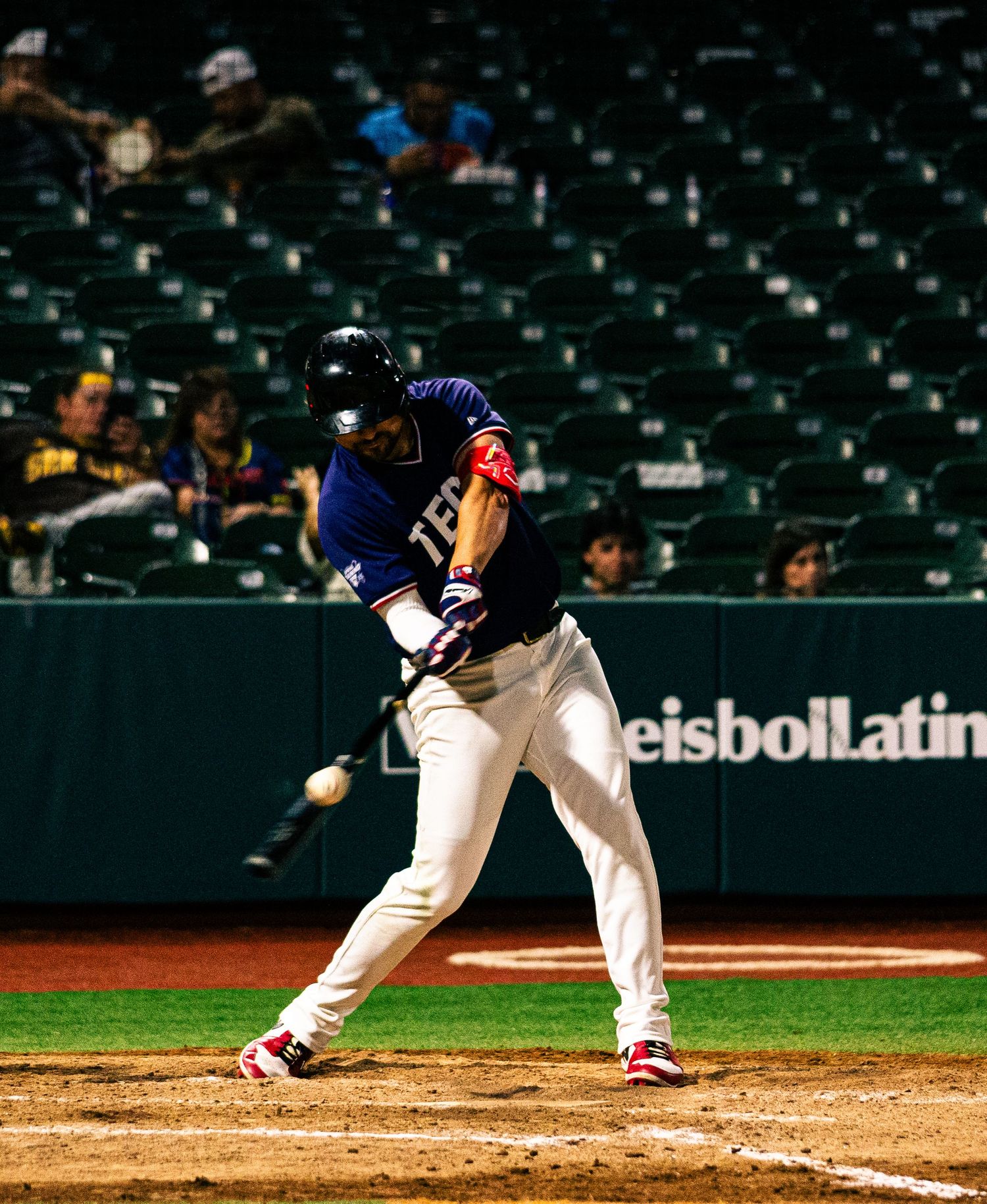 Baseball batter in blue uniform makes contact with pitch during a night game at a professional stadium.