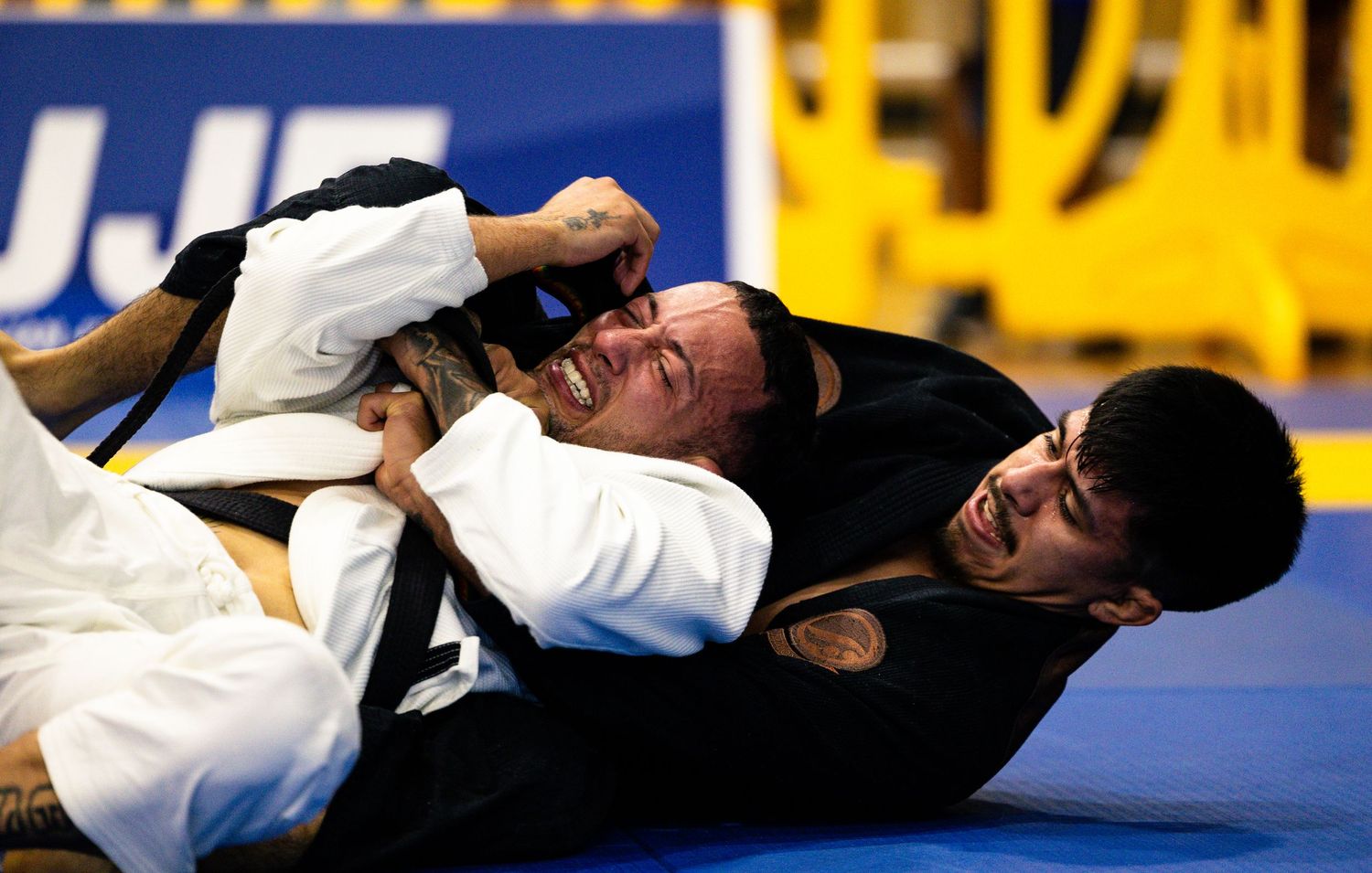 Two BJJ competitors grapple on the mat during an IBJJF tournament match.