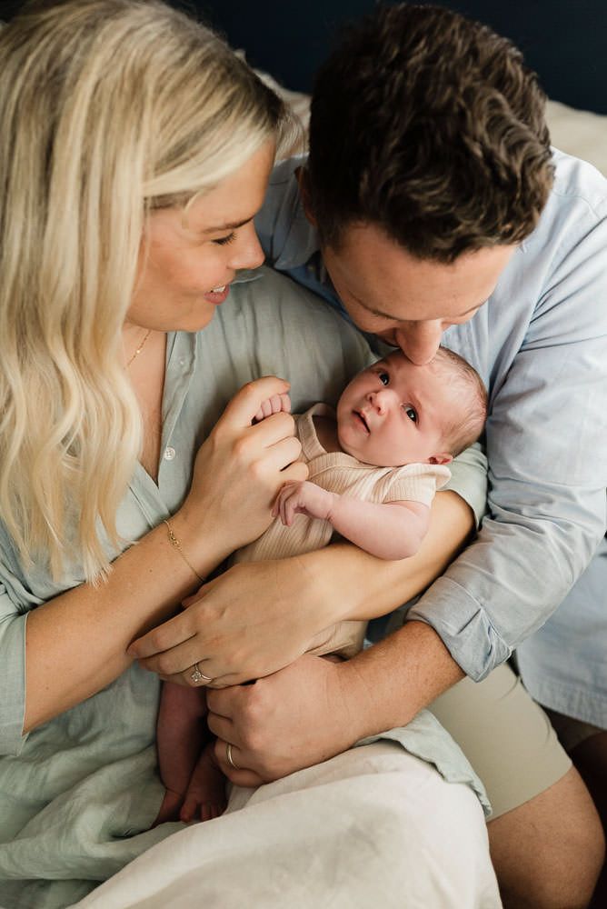 Parents lovingly hold and look down at their newborn baby during an intimate lifestyle photoshoot.