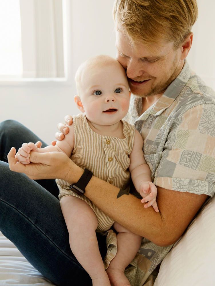 Parent and baby share tender moments together while relaxing on light colored bedding.