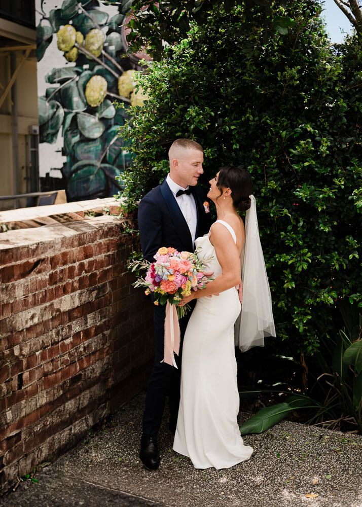 A romantic wedding couple shares intimate moments against a brick wall and garden backdrop during their special day.