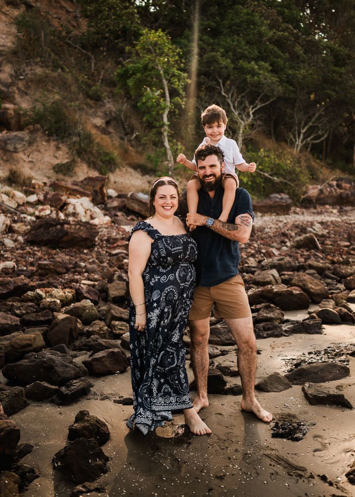 A couple shares playful moments together while sitting on rocky terrain near a shoreline.