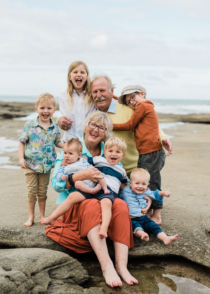 Family group sitting together on coastal rocks at the beach during a cloudy day.