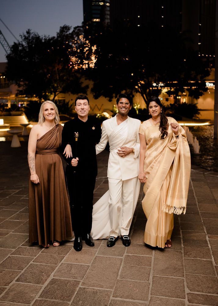 Group of people in formal attire posing together on stone patio at dusk during an evening celebration.