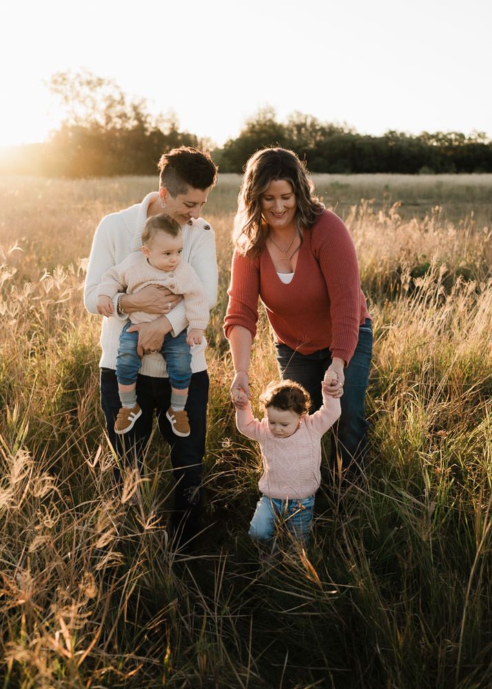 A family enjoys a tender moment together in a golden sunlit field with tall grass at sunset.