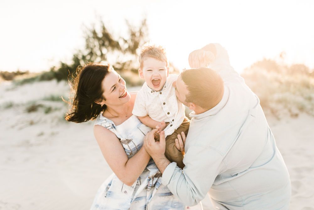 A family shares a joyful moment together on a sandy beach at sunset with golden light streaming through.