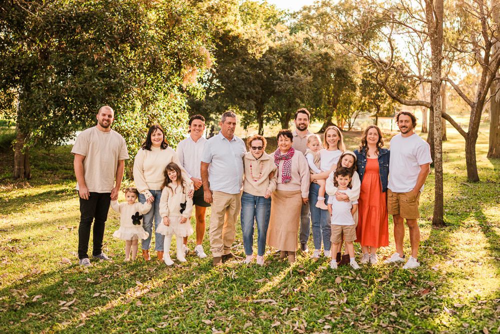 A group of people wearing coordinated pastel outfits pose together in a sunlit outdoor setting during golden hour.
