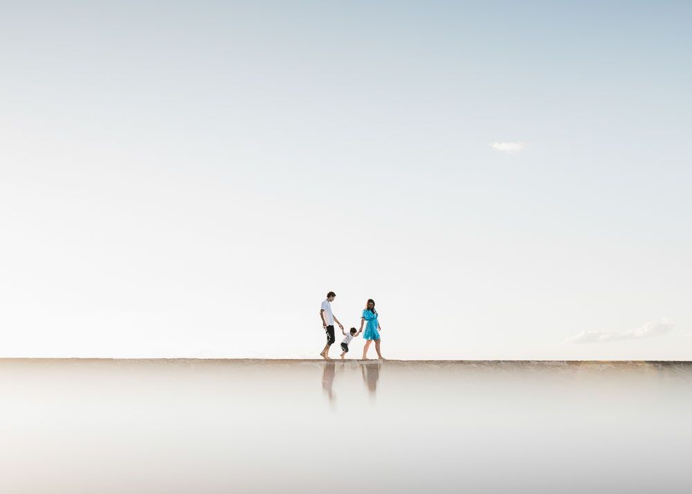 Two distant figures walk along a misty beach shoreline during a serene, overcast day.