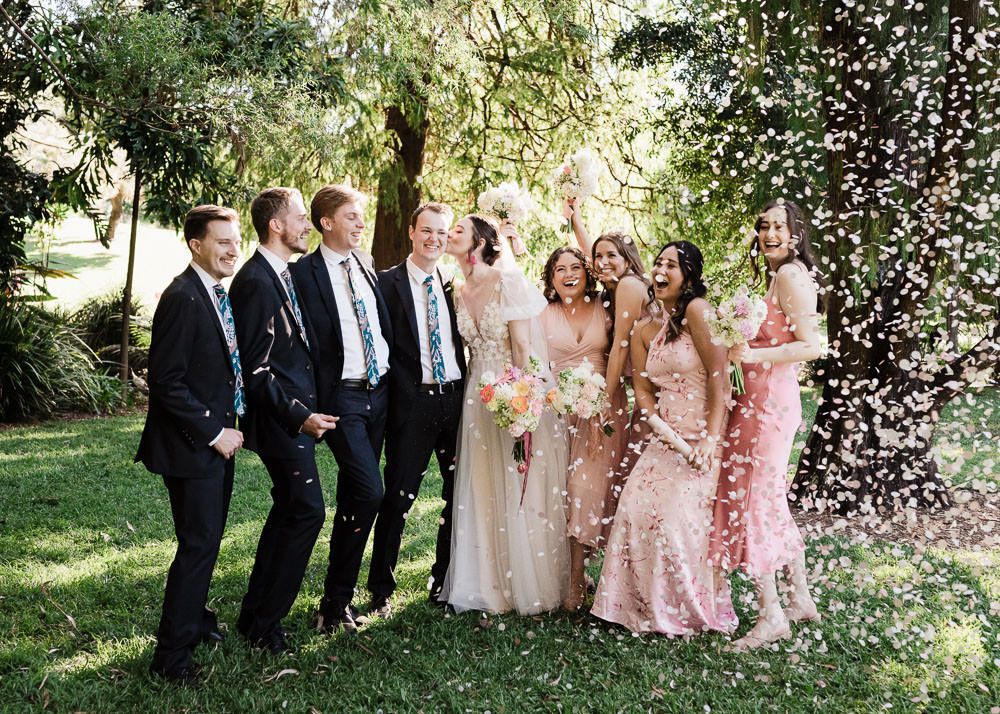 Wedding party celebrates with confetti in a lush garden setting during golden hour.