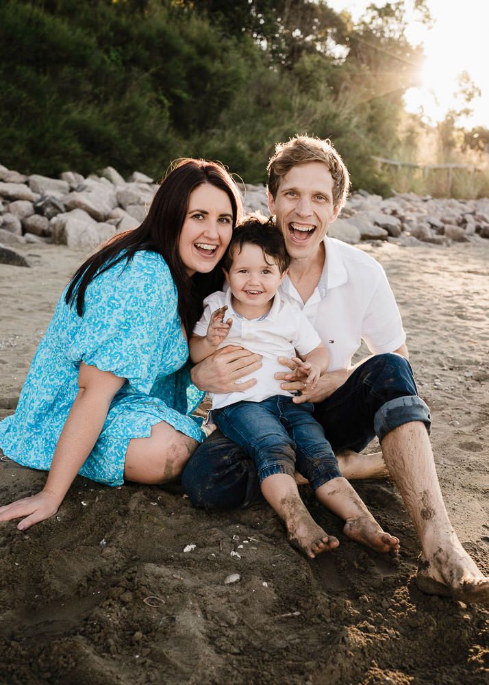 Family relaxes together on a rocky beach at sunset creating candid moments in casual attire.