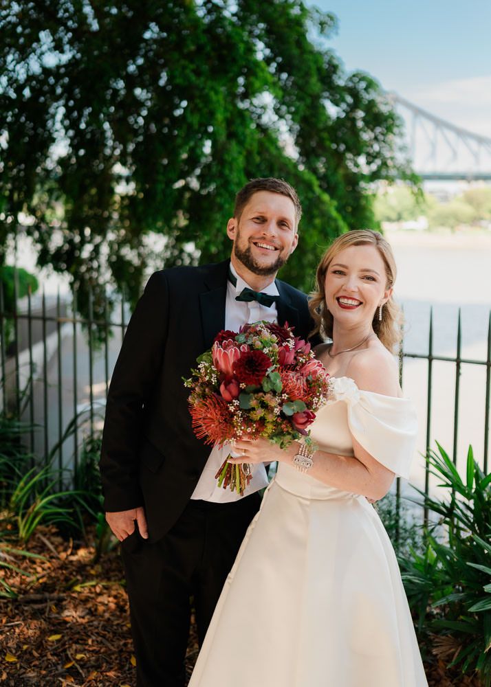 Newlyweds share joyful laughter while holding vibrant autumn-colored bouquets in an outdoor garden setting.
