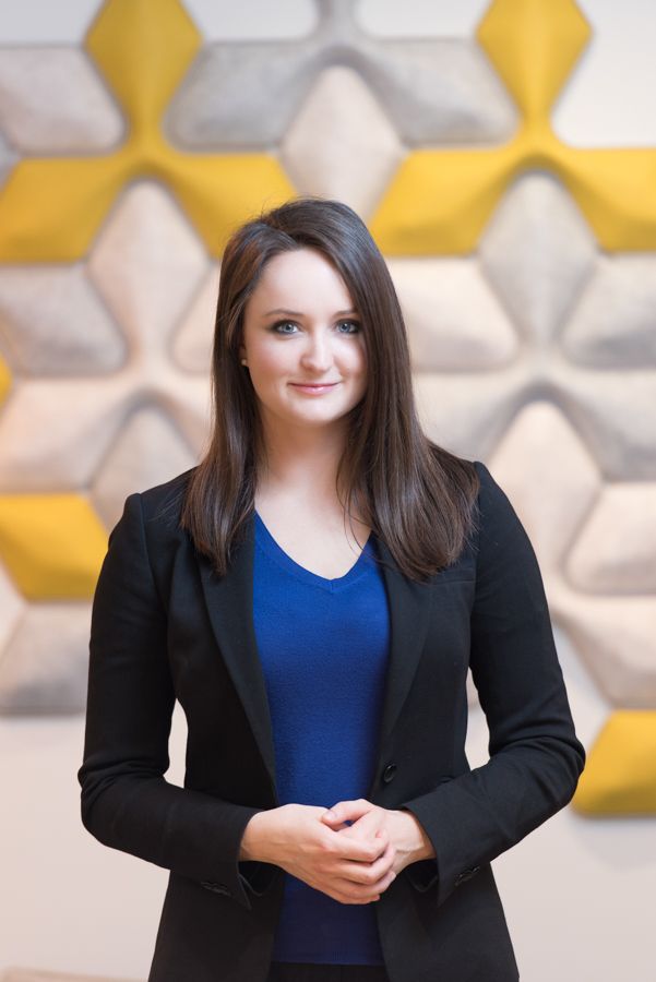 Professional wearing a black blazer and royal blue top poses against a geometric yellow and white background.