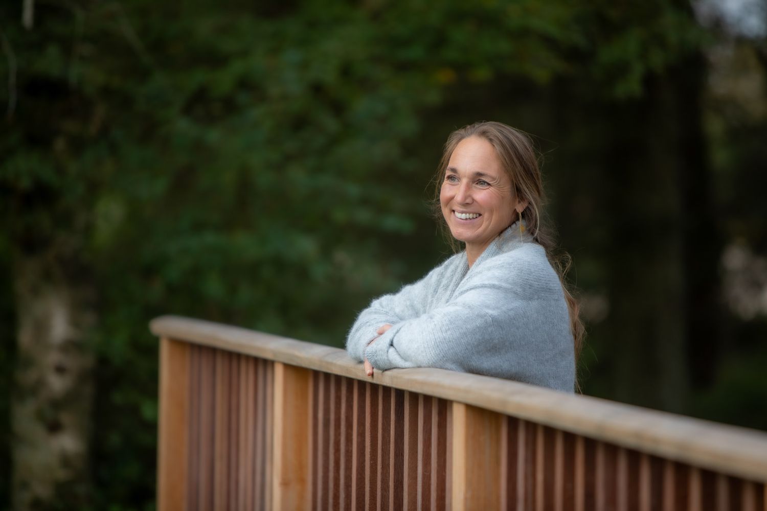 Person in light blue sweater sitting on wooden deck railing with natural scenery in background.
