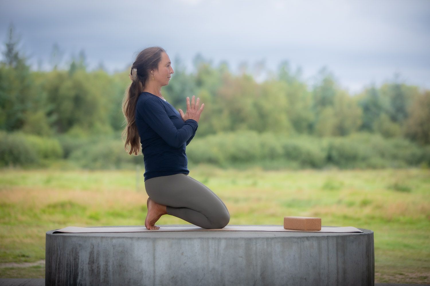 Person performing yoga poses on a concrete platform outdoors in a natural setting with trees in background.