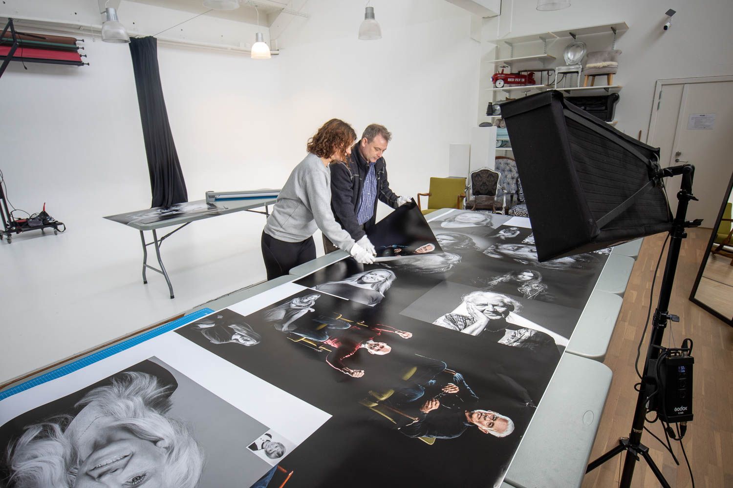 Two people reviewing printed photographs laid out on a large table.