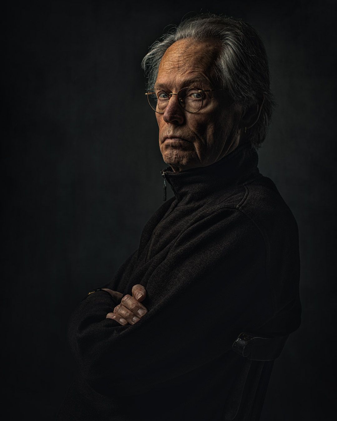 Dramatic portrait of elderly person in black clothing against dark background.
