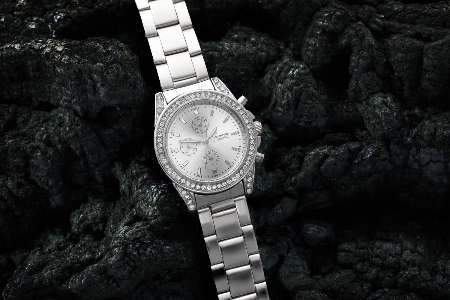 Luxury silver watches displayed on dark stone background with dramatic lighting.