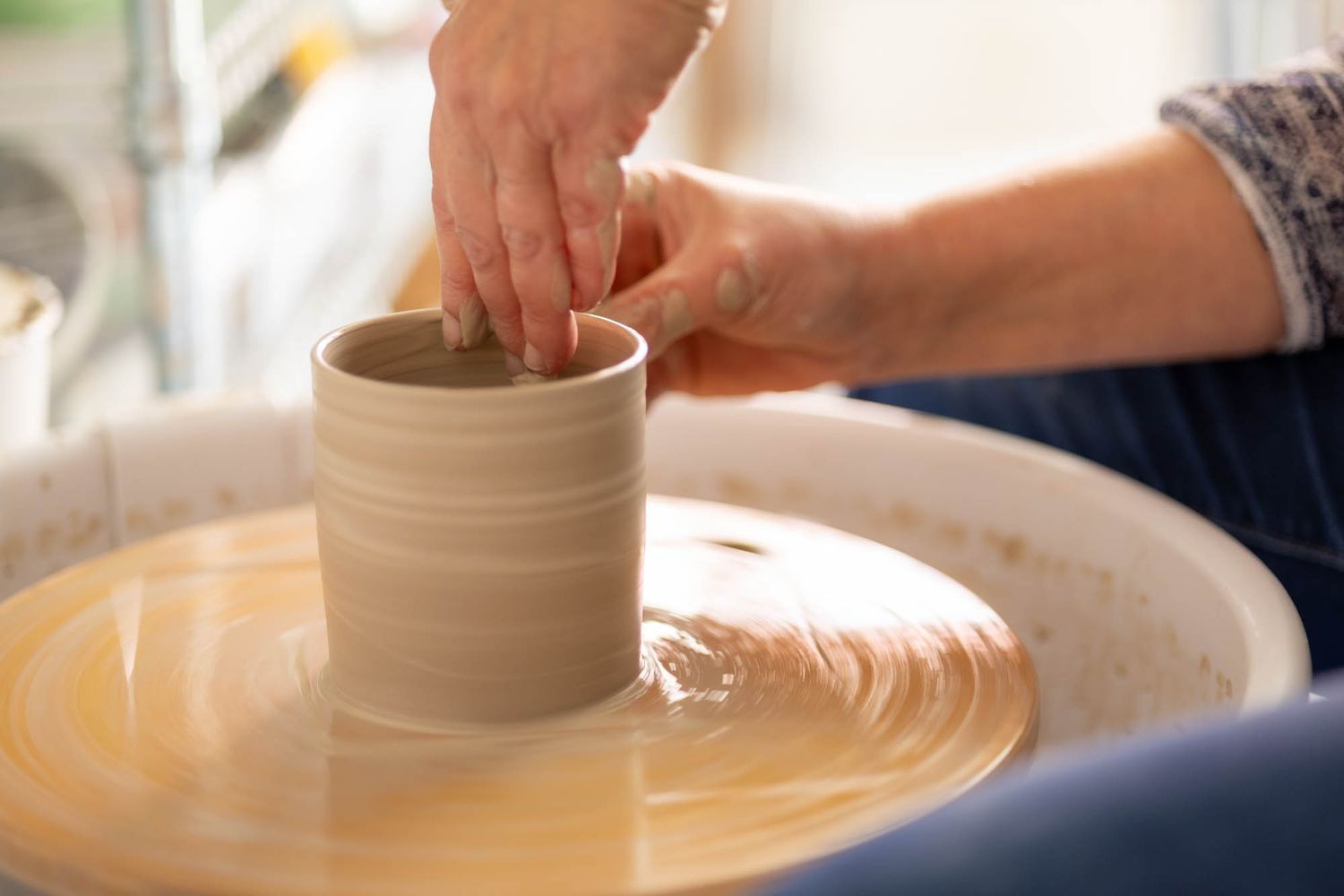 Close-up of hands shaping clay on a pottery wheel with wet clay visible.